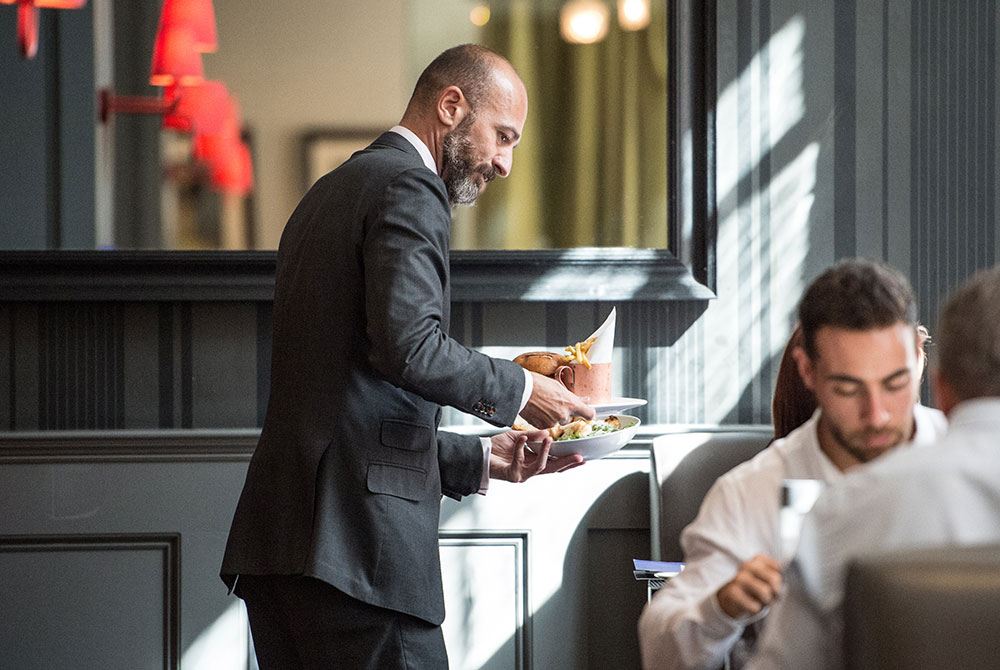 Waiter bringing out tasty dishes to hotel guests